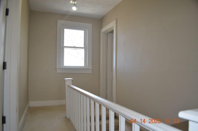 hall featuring baseboards, light colored carpet, and an upstairs landing