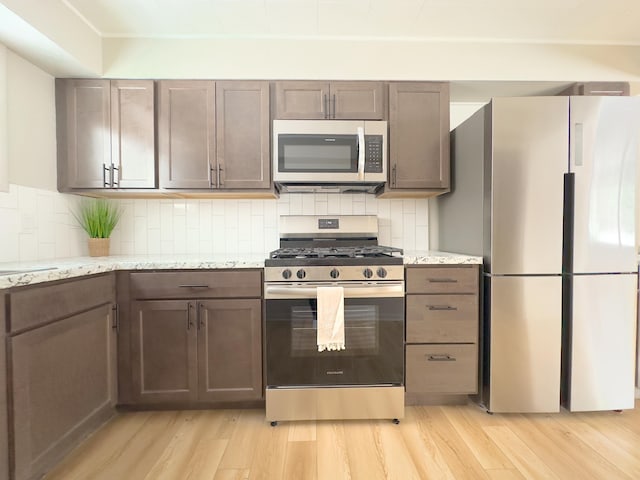 kitchen with stainless steel appliances, light stone countertops, light hardwood / wood-style floors, and decorative backsplash