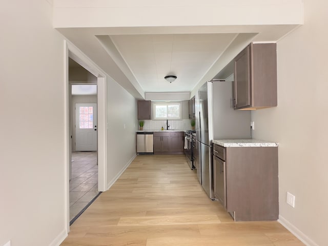 kitchen with stainless steel appliances, dark brown cabinets, sink, light hardwood / wood-style flooring, and backsplash