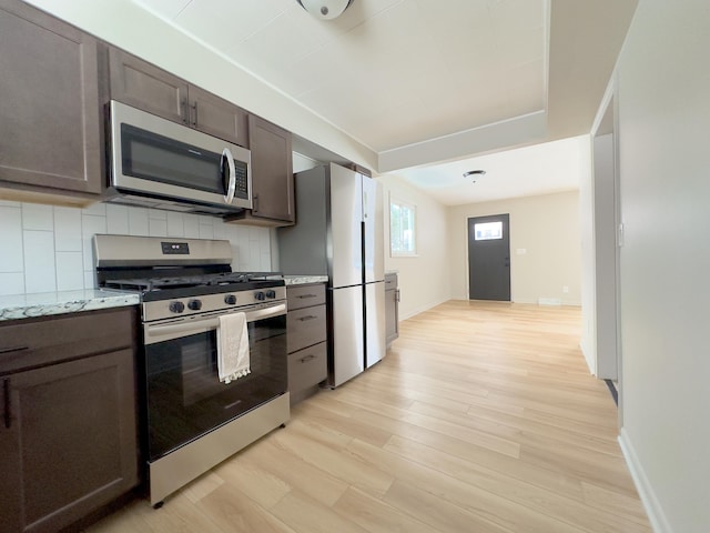 kitchen with light hardwood / wood-style floors, dark brown cabinetry, backsplash, light stone countertops, and appliances with stainless steel finishes