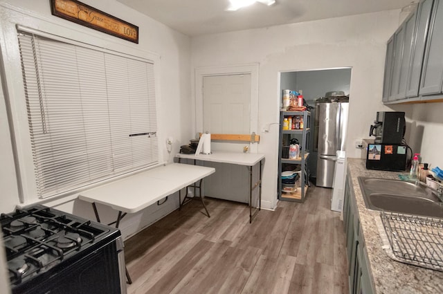 kitchen with gas stove, stainless steel refrigerator, gray cabinetry, sink, and light wood-type flooring