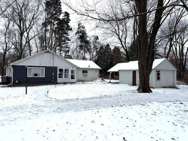 snow covered back of property with an outbuilding, a garage, and a carport