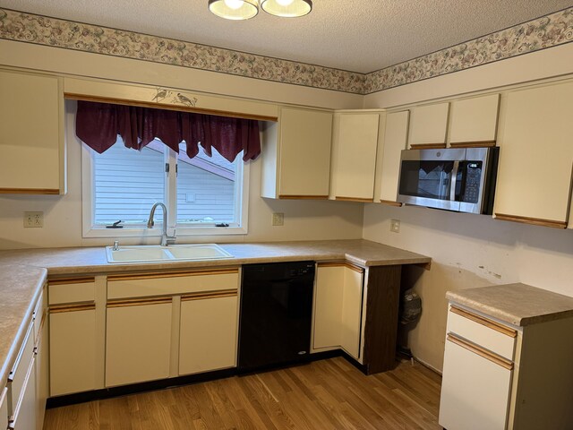 kitchen featuring a textured ceiling, cream cabinetry, black dishwasher, and sink