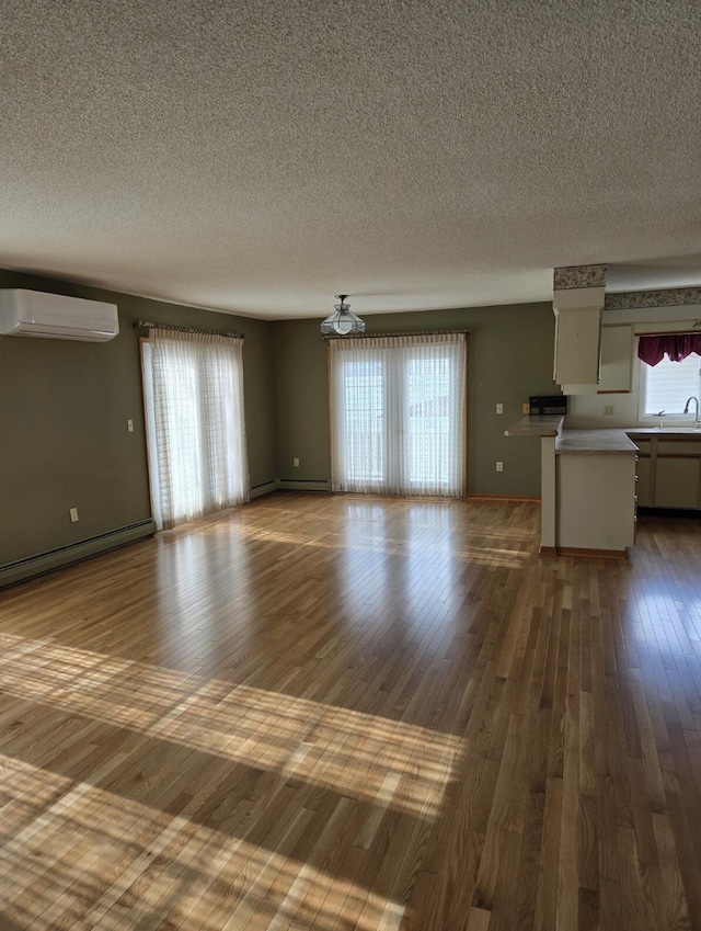 unfurnished living room featuring sink, a textured ceiling, hardwood / wood-style flooring, baseboard heating, and a wall mounted air conditioner