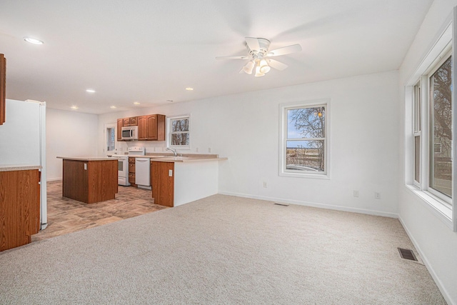 kitchen featuring white appliances, light carpet, a kitchen breakfast bar, a kitchen island, and kitchen peninsula