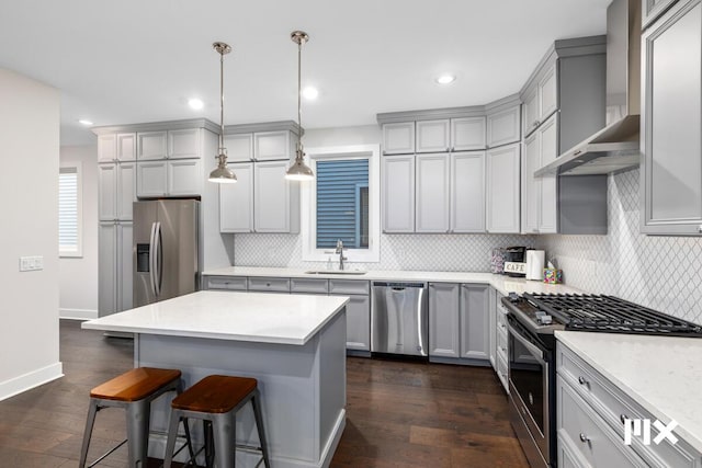 kitchen featuring wall chimney range hood, gray cabinets, stainless steel appliances, and a kitchen breakfast bar