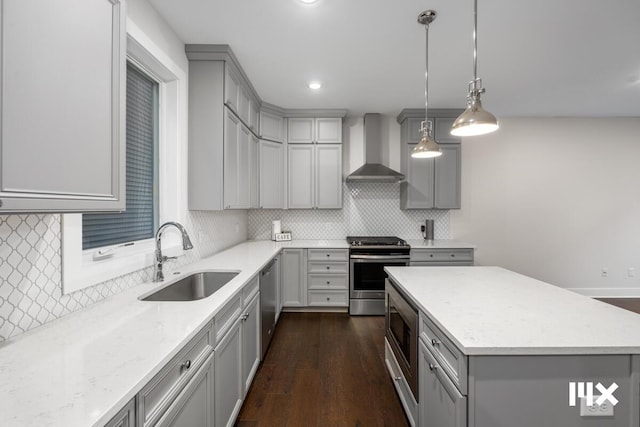 kitchen featuring gray cabinetry, a sink, appliances with stainless steel finishes, a center island, and wall chimney exhaust hood