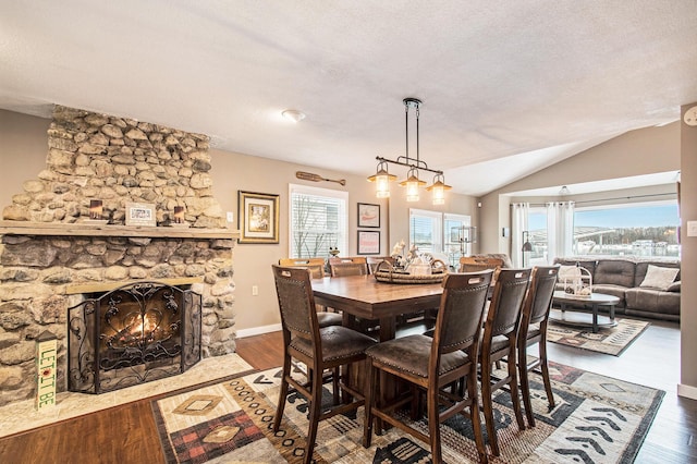 dining space with a textured ceiling, a stone fireplace, wood-type flooring, and lofted ceiling