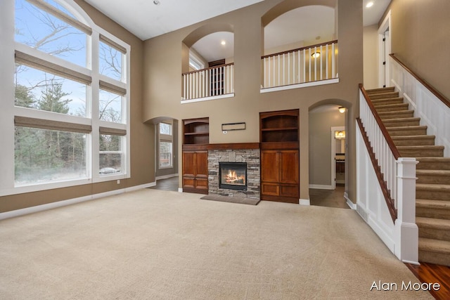 unfurnished living room with carpet, a towering ceiling, a stone fireplace, and built in features