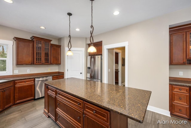 kitchen featuring dark stone counters, hanging light fixtures, appliances with stainless steel finishes, a kitchen island, and a kitchen bar