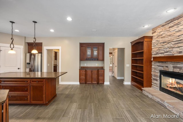 kitchen with a fireplace, stainless steel fridge with ice dispenser, hanging light fixtures, and dark stone counters