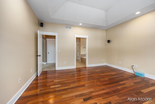 unfurnished bedroom featuring a tray ceiling, dark wood-type flooring, and ensuite bathroom