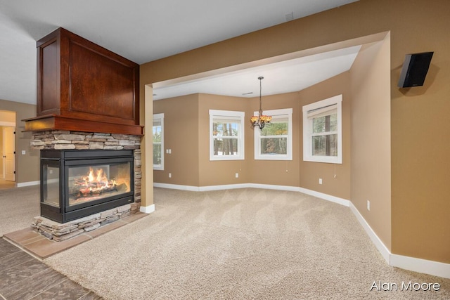 unfurnished living room featuring a stone fireplace, carpet floors, and an inviting chandelier