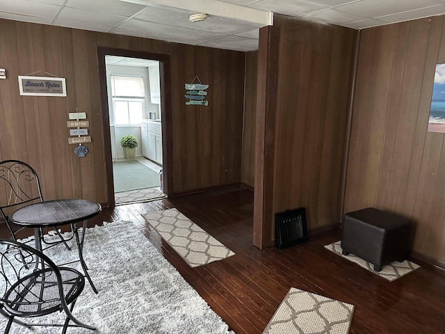 interior space with dark hardwood / wood-style floors, a drop ceiling, and wood walls