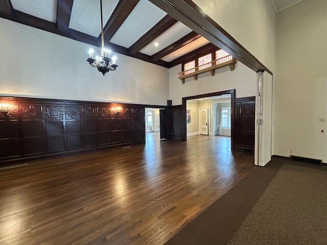 unfurnished living room featuring beamed ceiling, dark hardwood / wood-style floors, and a notable chandelier