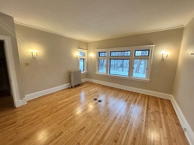 empty room featuring radiator, light wood-type flooring, and ornamental molding