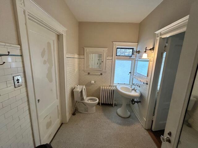 bathroom featuring tile patterned floors, radiator heating unit, tile walls, and toilet