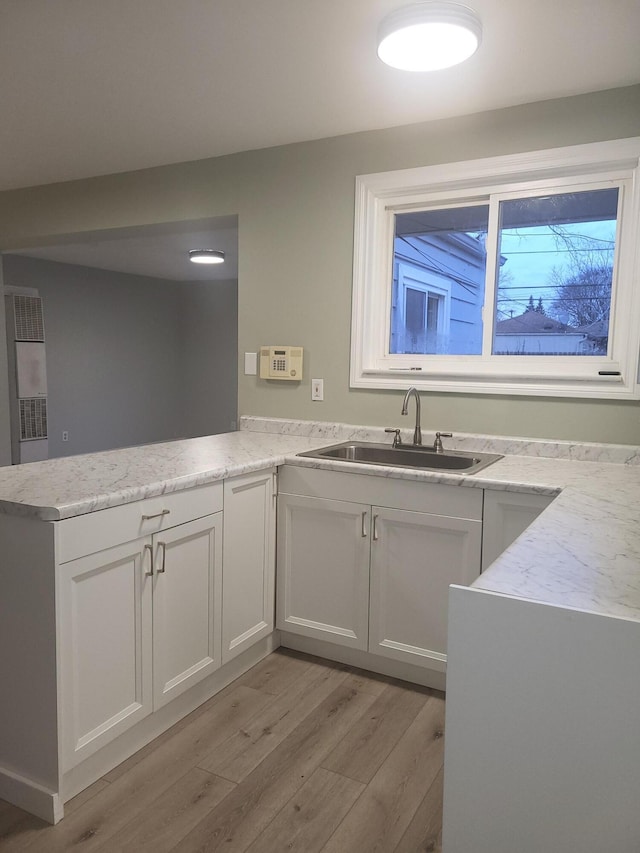 kitchen featuring kitchen peninsula, white cabinetry, light stone countertops, and sink