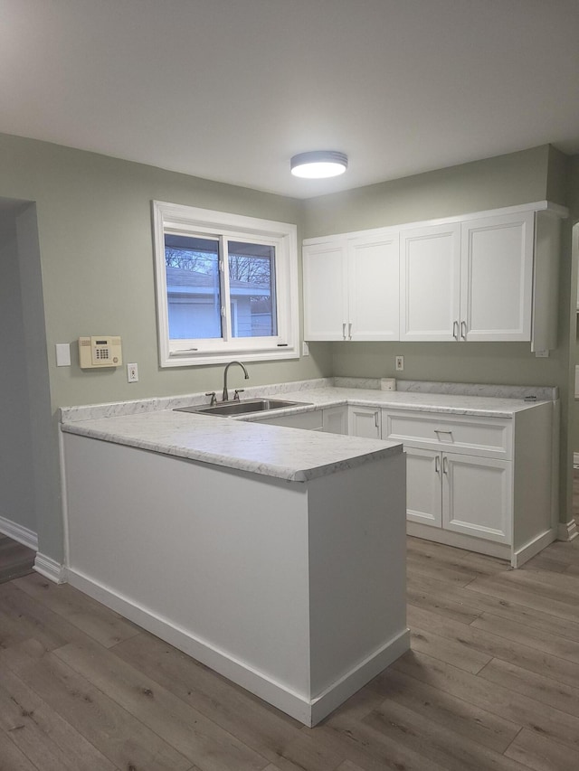 kitchen with kitchen peninsula, white cabinetry, sink, and light hardwood / wood-style flooring