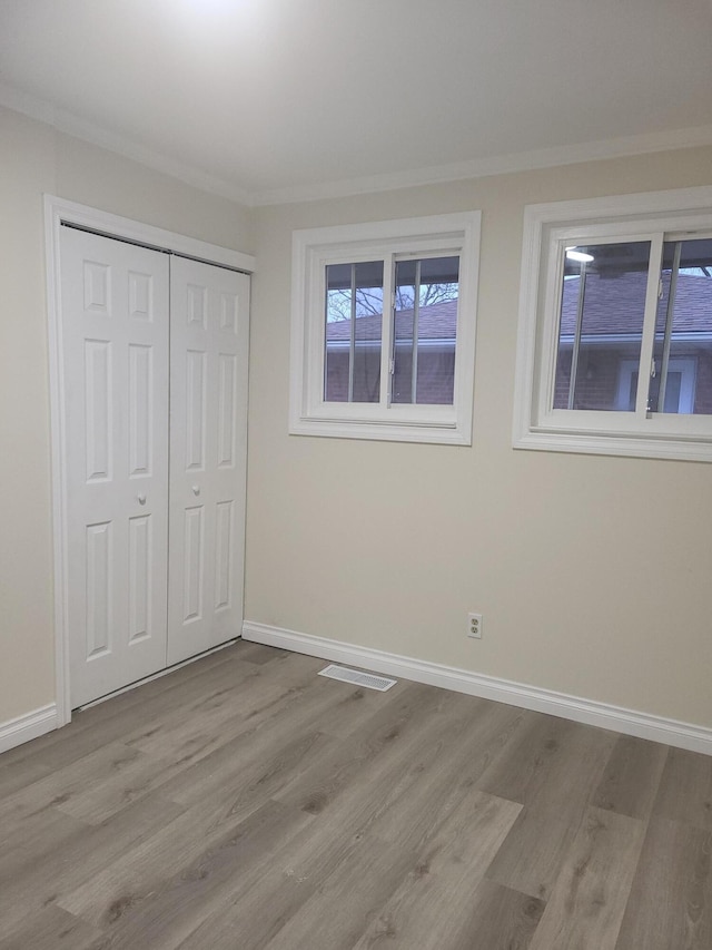 unfurnished bedroom featuring light hardwood / wood-style flooring, a closet, and crown molding