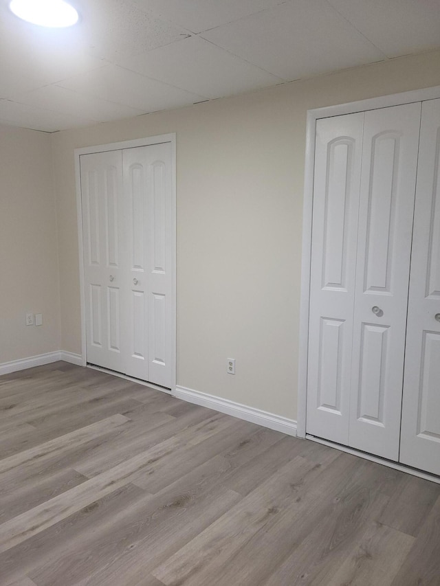 unfurnished bedroom featuring a paneled ceiling, light hardwood / wood-style floors, and multiple closets