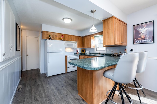 kitchen with kitchen peninsula, white appliances, sink, dark hardwood / wood-style floors, and hanging light fixtures