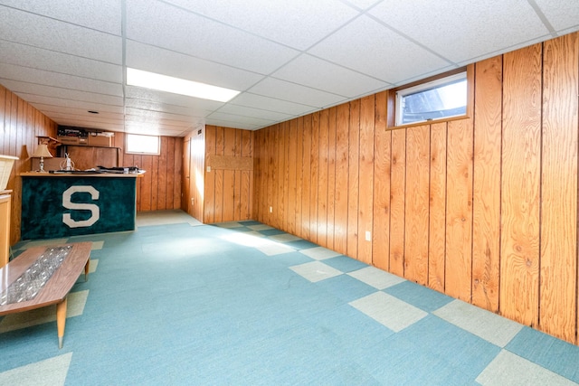 basement with a drop ceiling and wooden walls