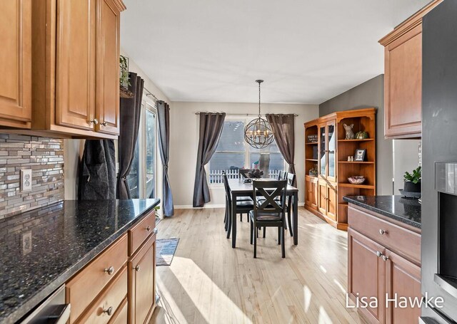 kitchen featuring hanging light fixtures, backsplash, dark stone counters, a chandelier, and light wood-type flooring