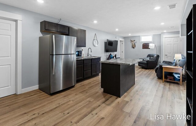 kitchen featuring light stone countertops, appliances with stainless steel finishes, a kitchen island with sink, sink, and light hardwood / wood-style flooring