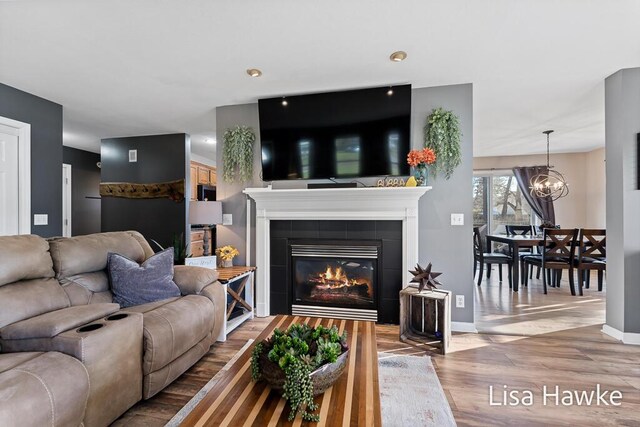 living room with hardwood / wood-style flooring, a tile fireplace, and an inviting chandelier