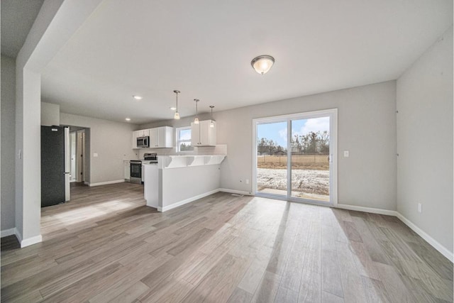 kitchen with appliances with stainless steel finishes, decorative light fixtures, white cabinets, light hardwood / wood-style floors, and kitchen peninsula