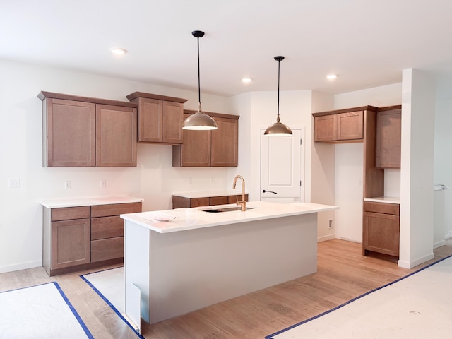 kitchen featuring decorative light fixtures, an island with sink, light hardwood / wood-style floors, and sink