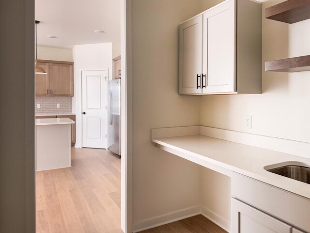 kitchen with tasteful backsplash, stainless steel fridge, built in desk, and light hardwood / wood-style flooring