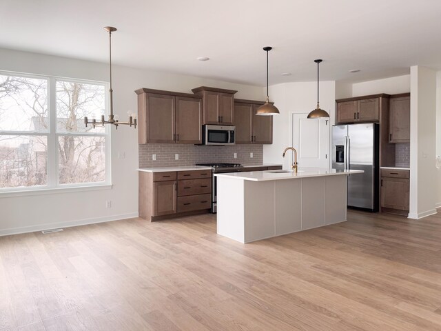 kitchen featuring pendant lighting, sink, a kitchen island with sink, stainless steel appliances, and light wood-type flooring