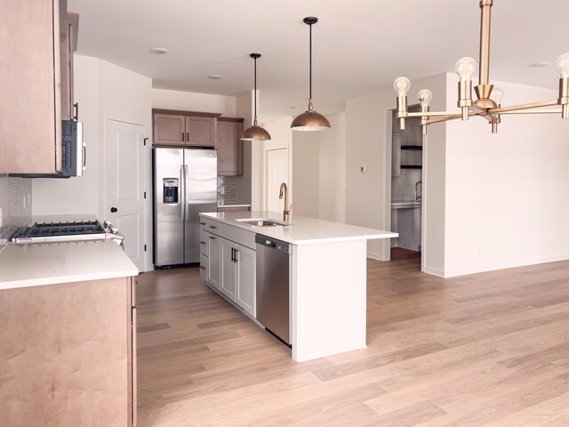 kitchen featuring sink, hanging light fixtures, a kitchen island with sink, stainless steel appliances, and light wood-type flooring