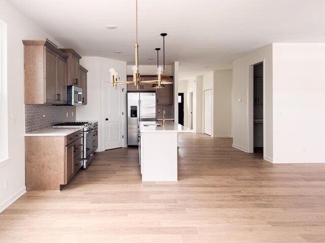 kitchen featuring appliances with stainless steel finishes, decorative light fixtures, decorative backsplash, a center island with sink, and light hardwood / wood-style flooring