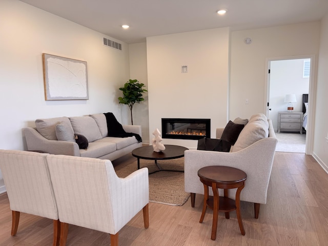 living area featuring recessed lighting, light wood-type flooring, visible vents, and a glass covered fireplace