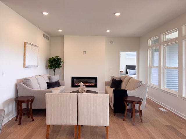 living room with visible vents, recessed lighting, baseboards, a glass covered fireplace, and light wood-style floors