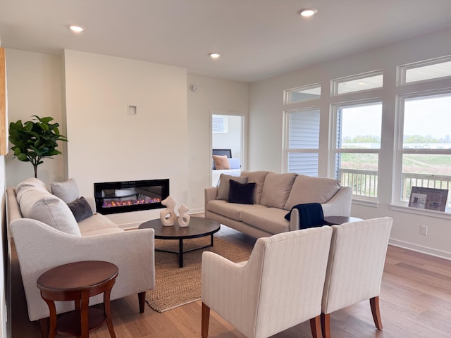 living room featuring light wood finished floors, a glass covered fireplace, recessed lighting, and plenty of natural light