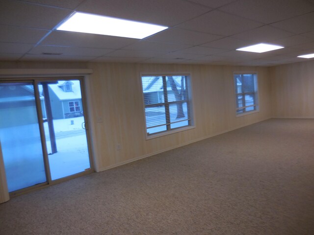 carpeted spare room with a paneled ceiling and wood walls