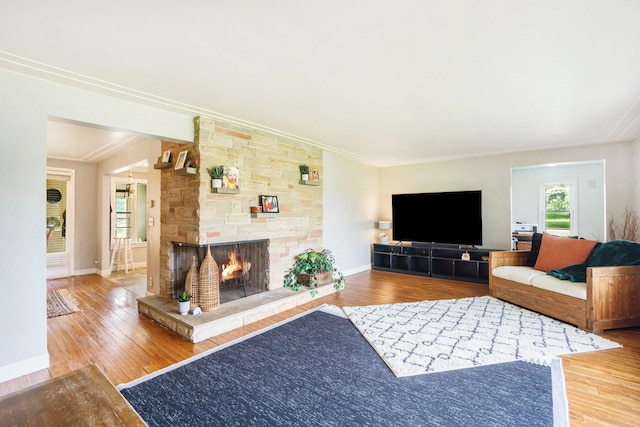 living room featuring hardwood / wood-style flooring, a stone fireplace, and crown molding