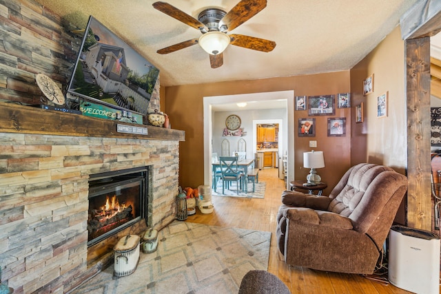 living room with a fireplace, a textured ceiling, light hardwood / wood-style floors, and ceiling fan