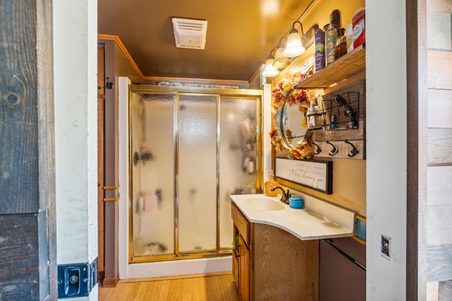 bathroom with a shower with door, vanity, wood-type flooring, and ornamental molding