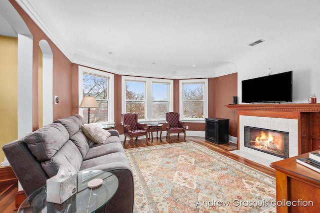 living room with a tiled fireplace, crown molding, and wood-type flooring