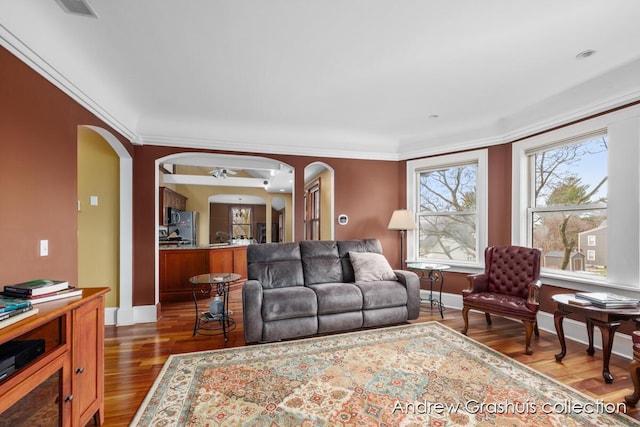 living room with crown molding, ceiling fan, and dark wood-type flooring