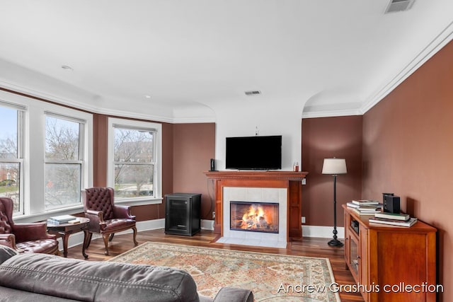 living room featuring a tile fireplace, crown molding, and hardwood / wood-style flooring