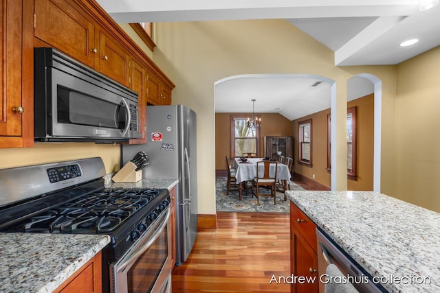 kitchen with light stone countertops, appliances with stainless steel finishes, light wood-type flooring, vaulted ceiling, and a chandelier