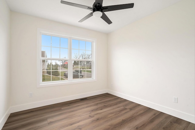 empty room with baseboards, dark wood-style floors, visible vents, and a ceiling fan