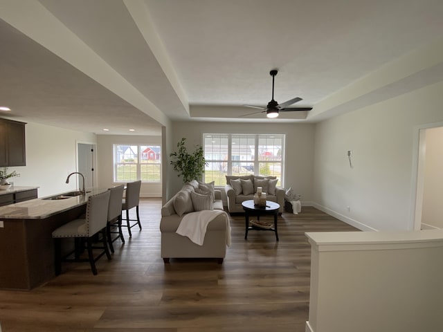 living area with baseboards, dark wood-style floors, a tray ceiling, and a ceiling fan