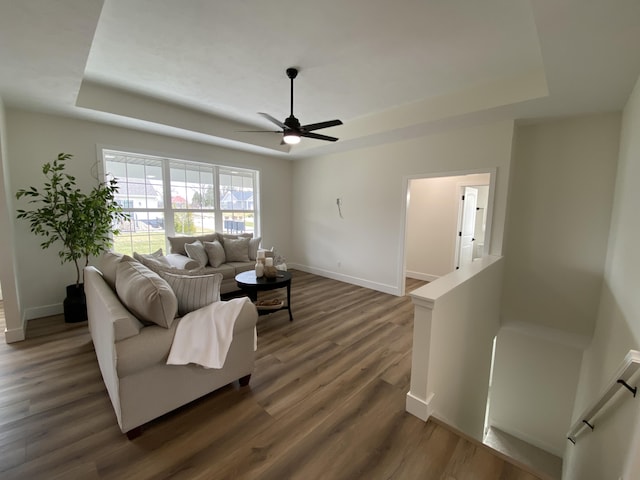 living room with a ceiling fan, a raised ceiling, baseboards, and wood finished floors